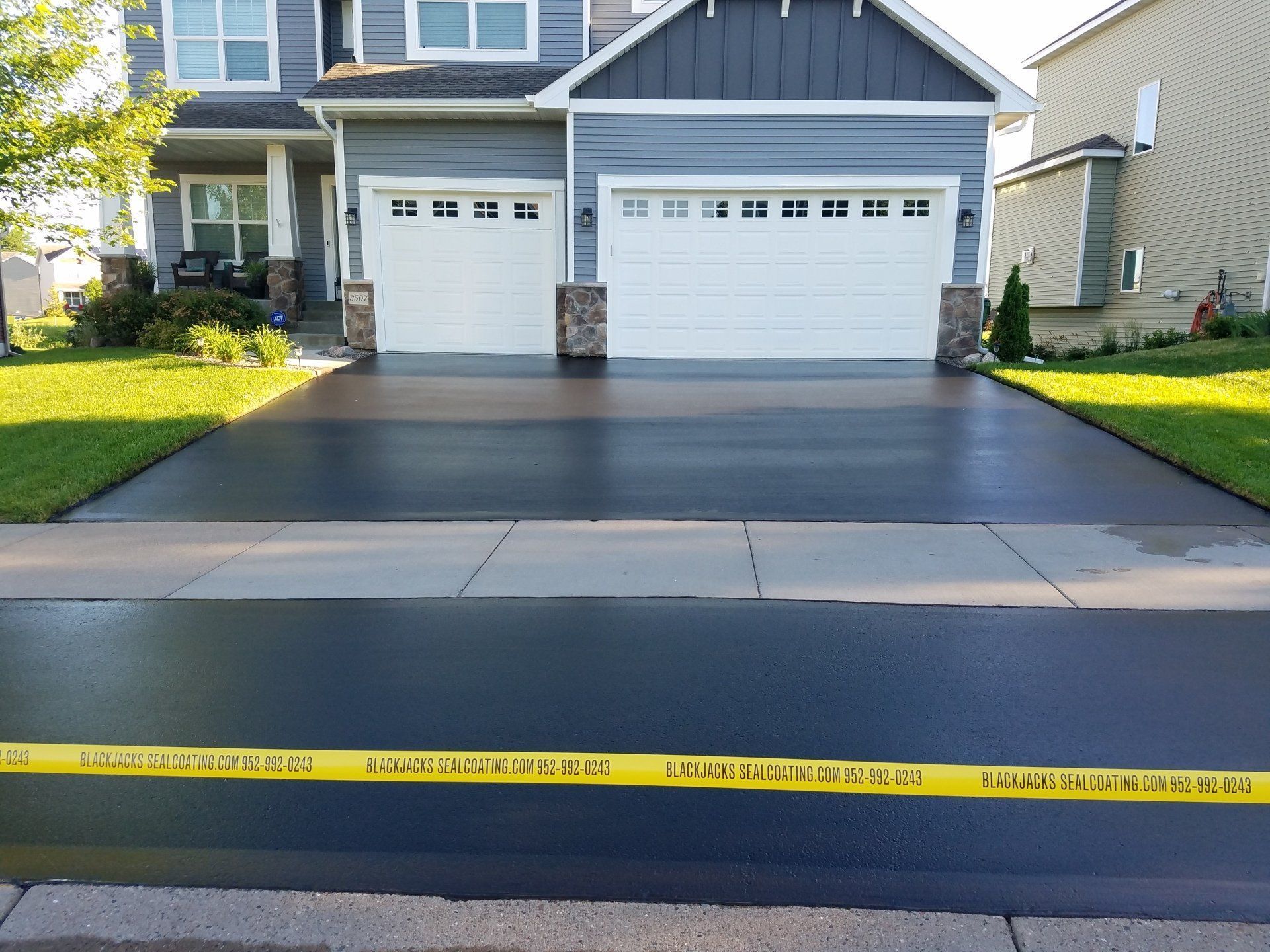 Two-car garage with fresh black driveway; yellow caution tape stretches across the front curb.