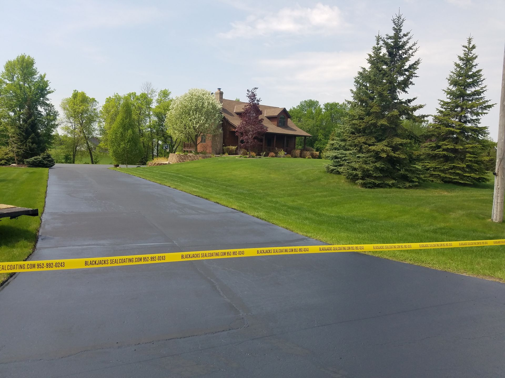 Yellow caution tape blocks a driveway leading to a house with a lawn and trees