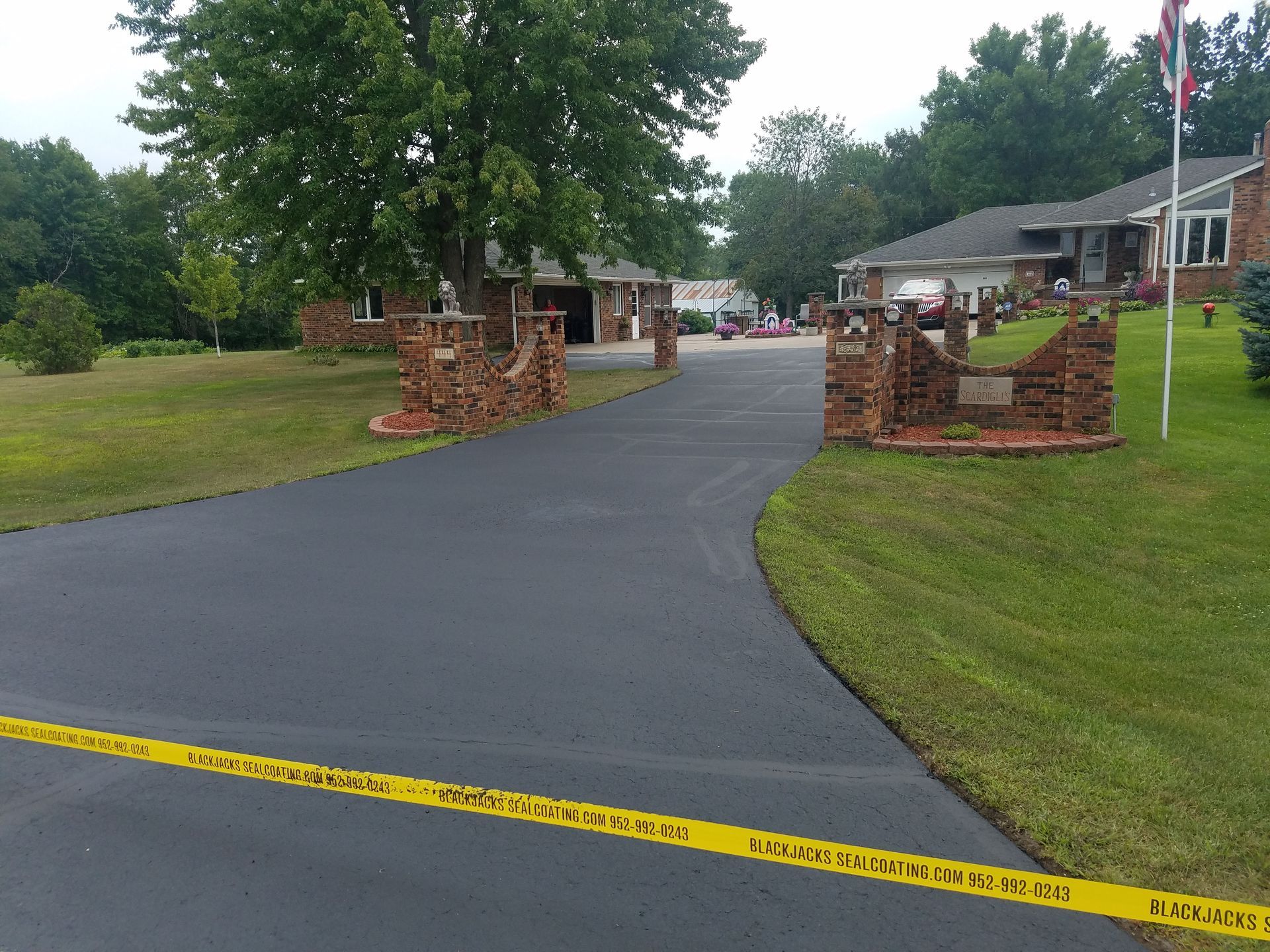 Yellow caution tape across a driveway entrance between brick pillars in a suburban neighborhood