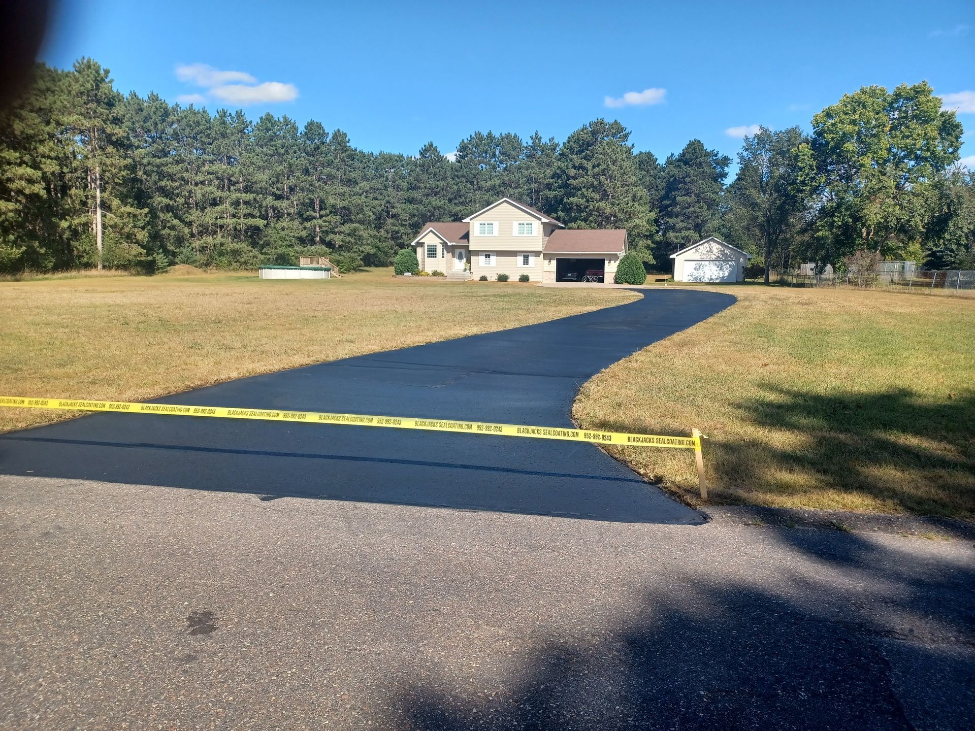 Freshly paved driveway leading to a beige house with a red-roofed porch in a grassy yard.