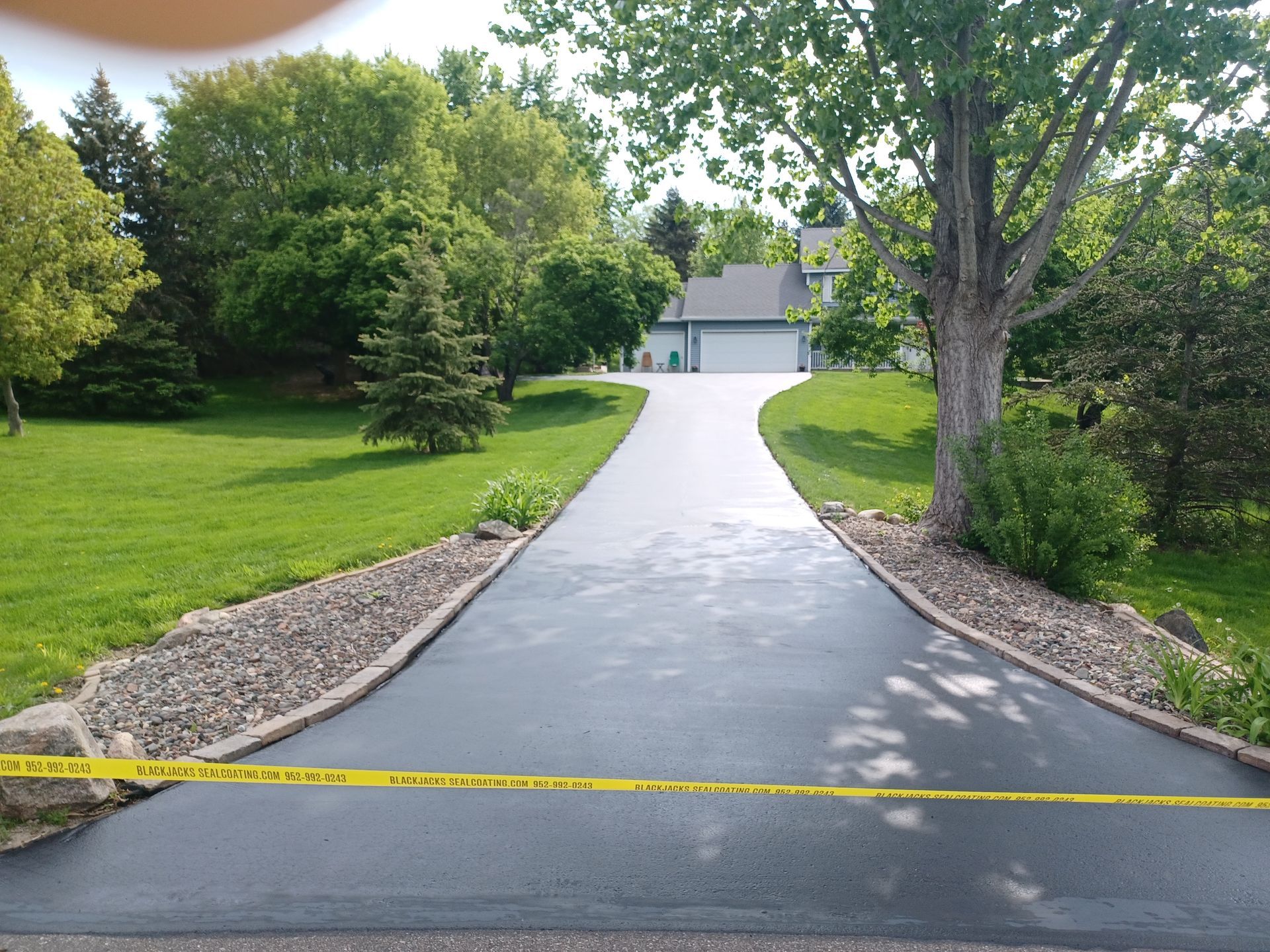 Curved asphalt driveway leading to a house, bordered by green lawn and trees