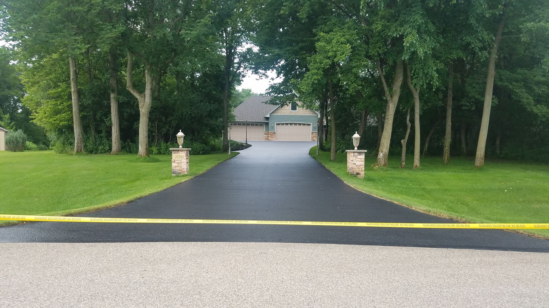 Tree-lined driveway leading to a house, with a yellow road edge in the foreground.