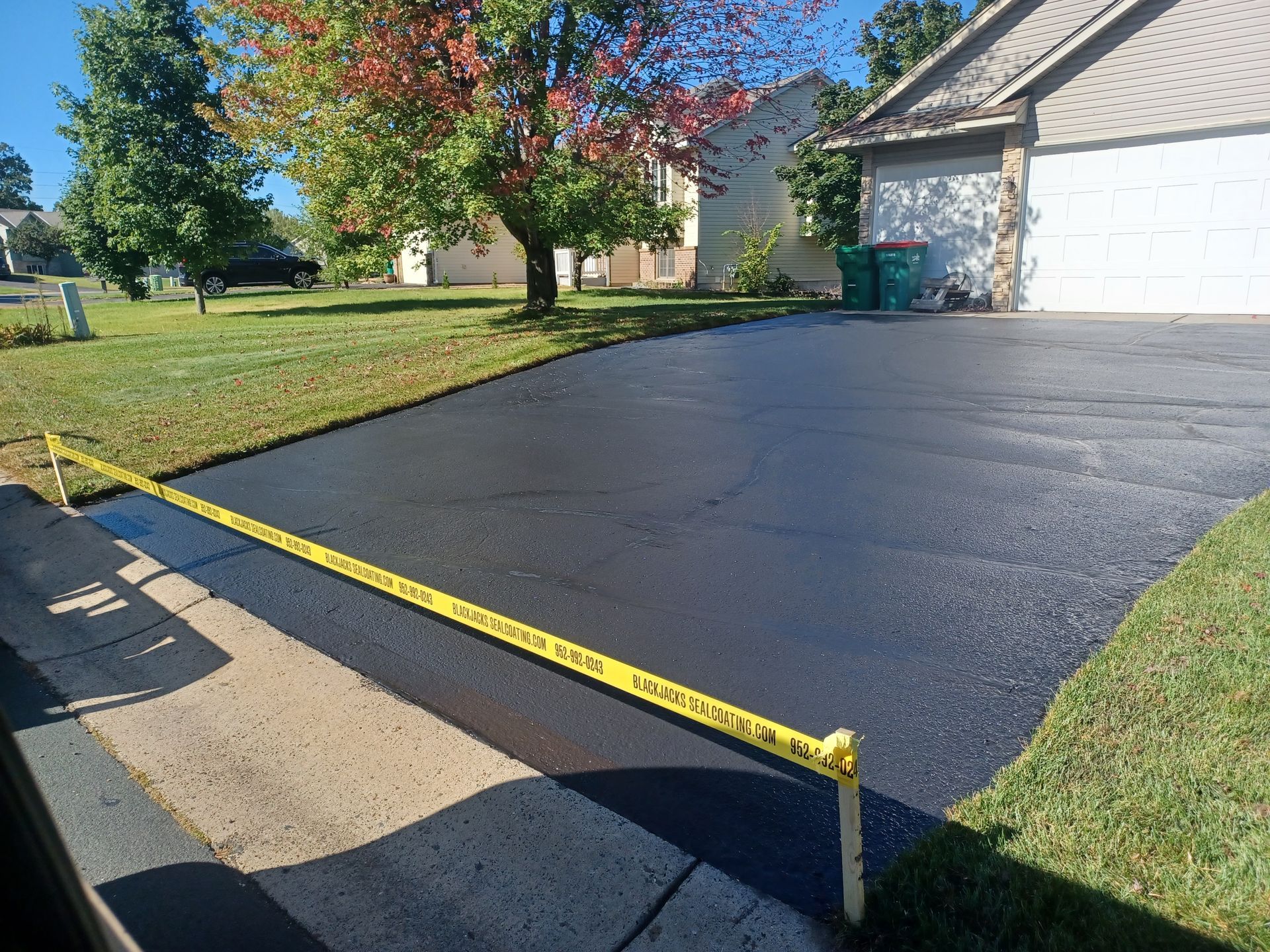 Freshly paved black driveway with yellow caution tape outside a suburban house