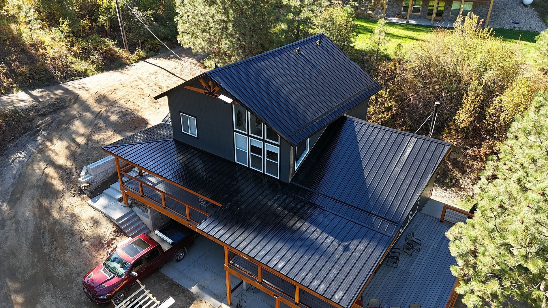 A black two-story house with a dark roof and orange trim, surrounded by trees and parked cars.