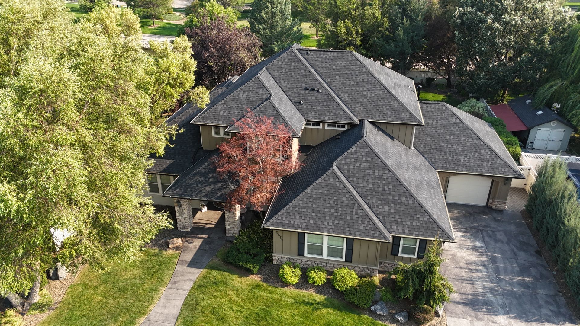 Aerial view of a large gray-roofed house surrounded by trees and a driveway