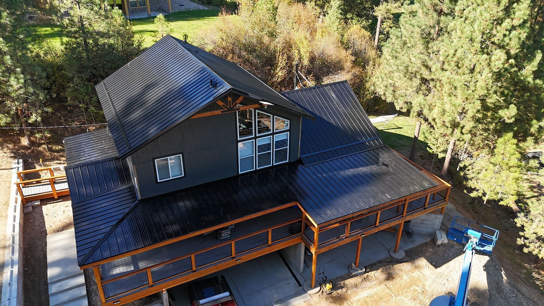 A dark-roofed house with a wraparound deck, set in a wooded area.