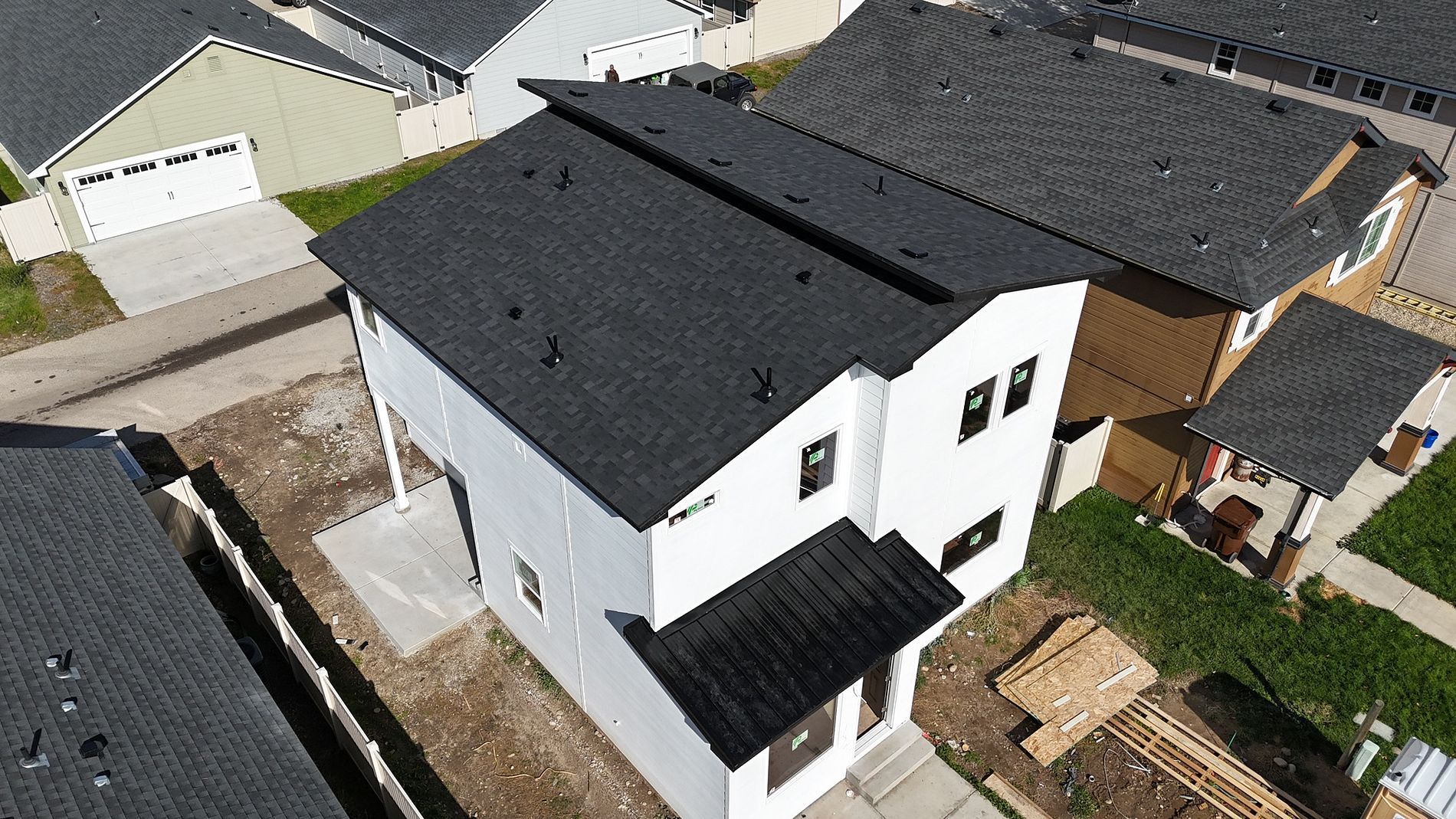Aerial view of a white two-story house with black roofing and trim, located in a neighborhood with similar houses.
