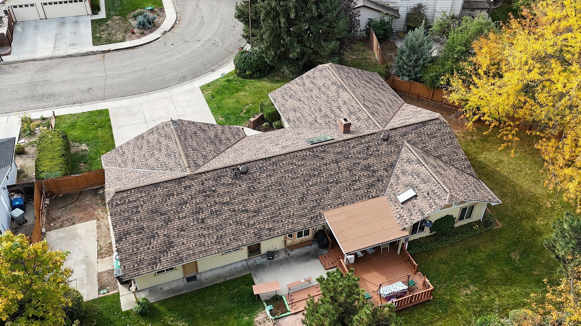 Aerial view of a house with a brown roof and a wooden deck surrounded by trees.