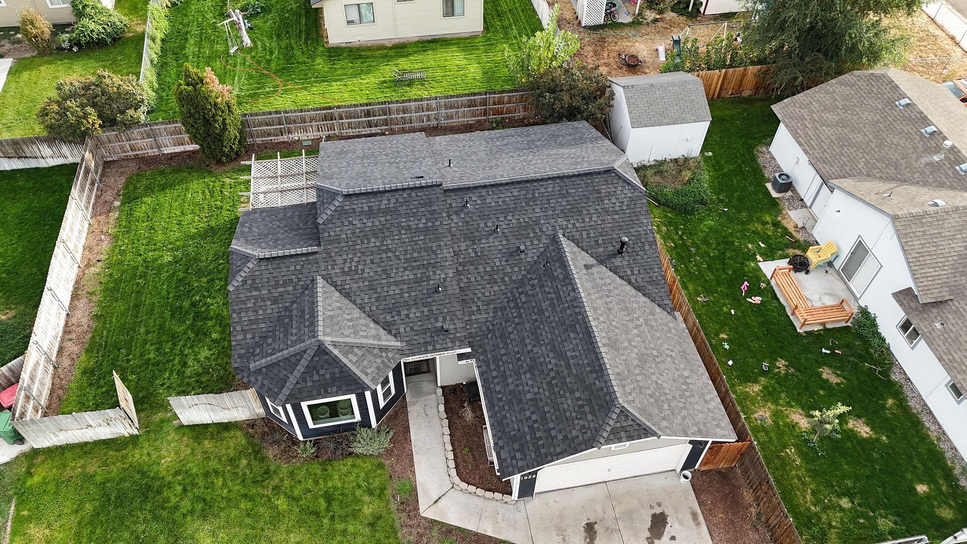 Overhead view of a house with a dark roof, green lawn, and concrete driveway.