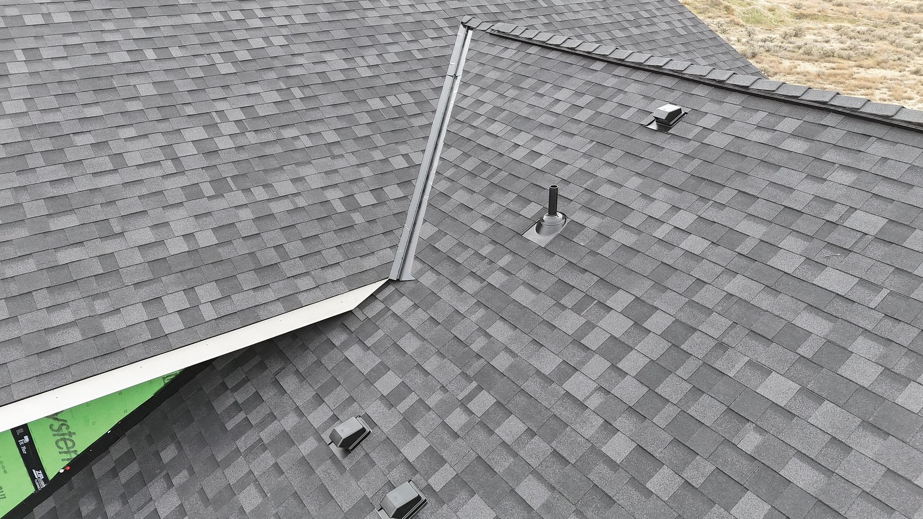 Gray asphalt shingle roof with vents and a metal chimney against a neutral sky.