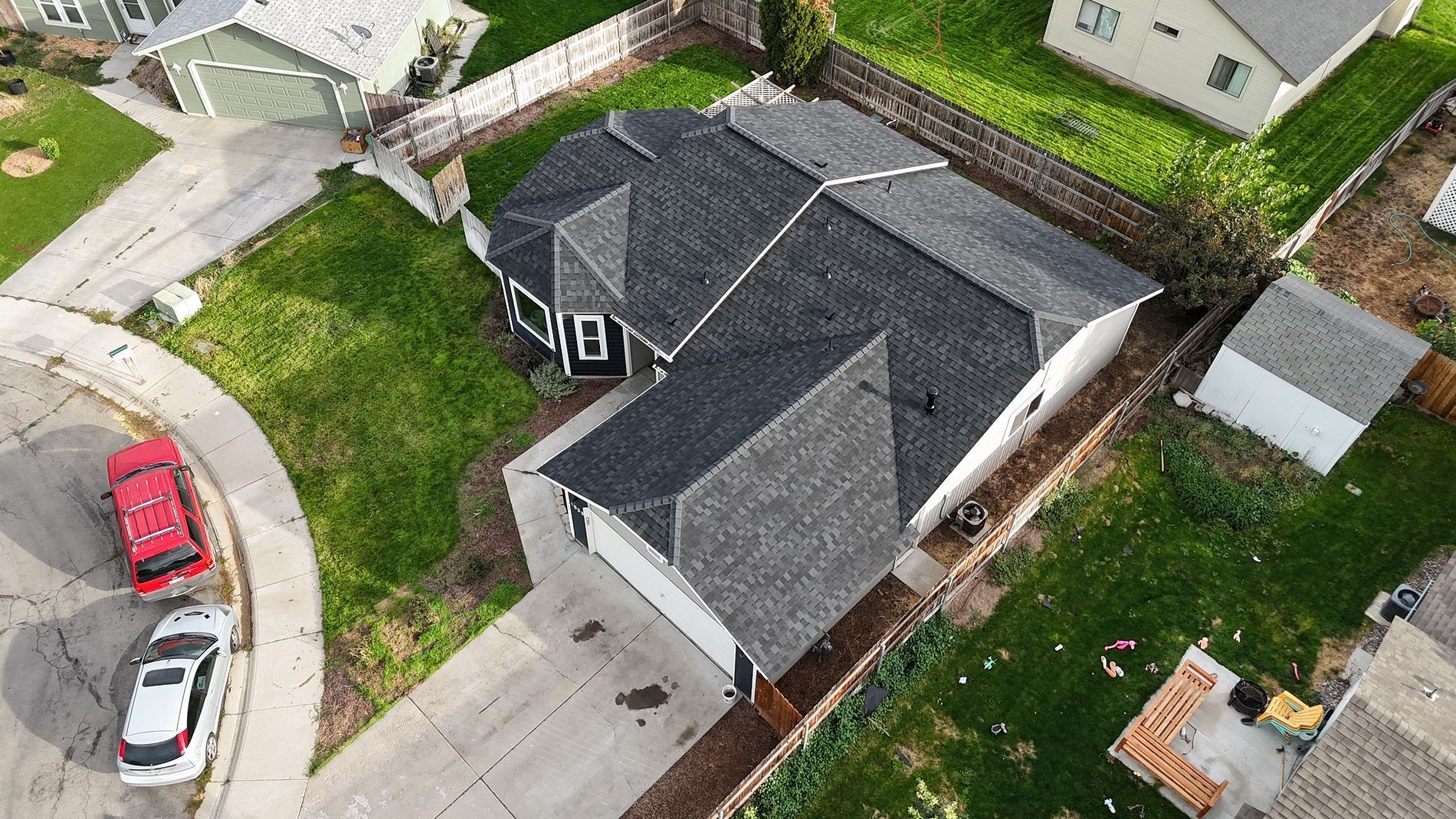 Aerial view of a gray-roofed house with a white garage door, surrounded by green grass and a driveway.