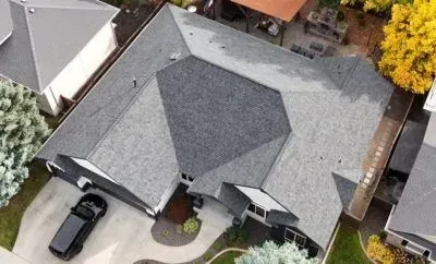 Aerial view of a gray-roofed house with a driveway, black car, and surrounding trees.