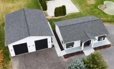 Aerial view of two gray-roofed houses with driveways and lawns on a residential street.
