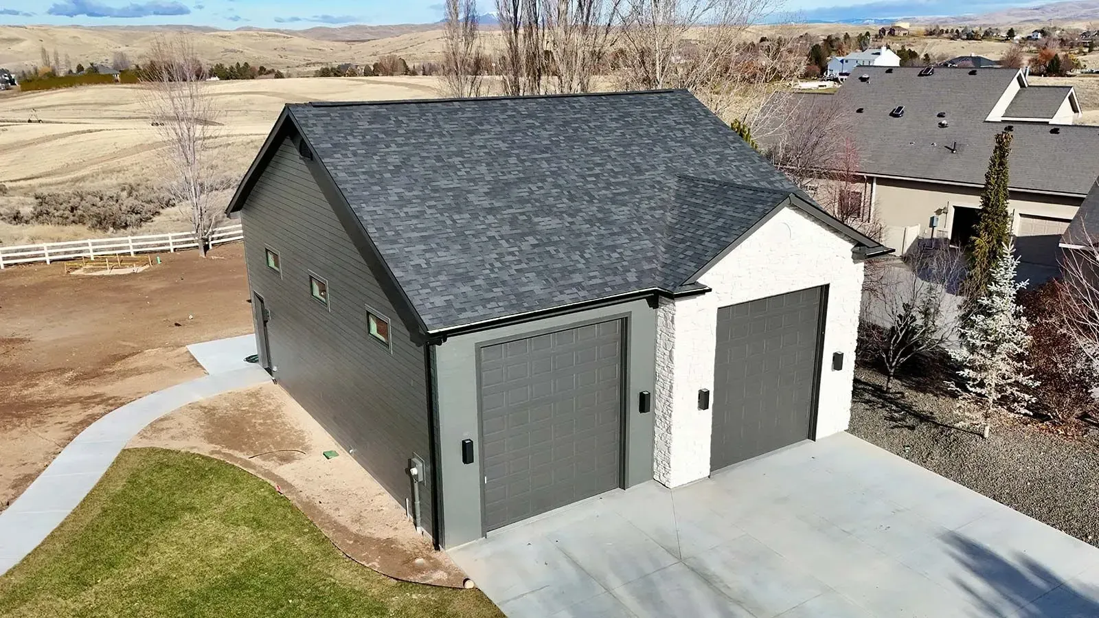 Detached gray two-car garage with dark roof and white door on a suburban lot