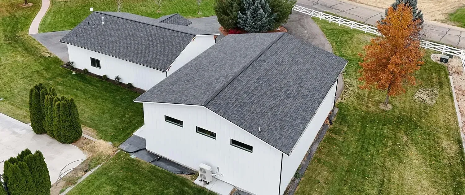Aerial view of a white house with a dark gray roof, detached garage, and grassy yard with trees