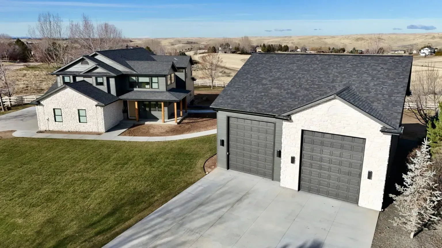 Two-story modern house with a detached two-car garage. Both have dark gray roofs and white brick exterior.