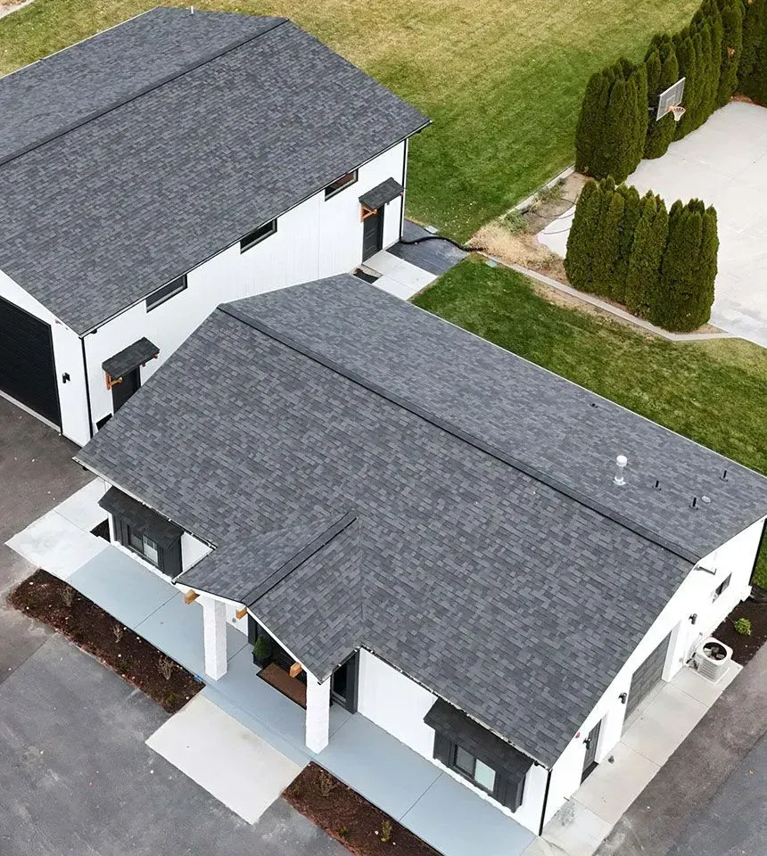 Two-story white house with black trim and dark gray roof. Adjacent building in the background. Green lawn.