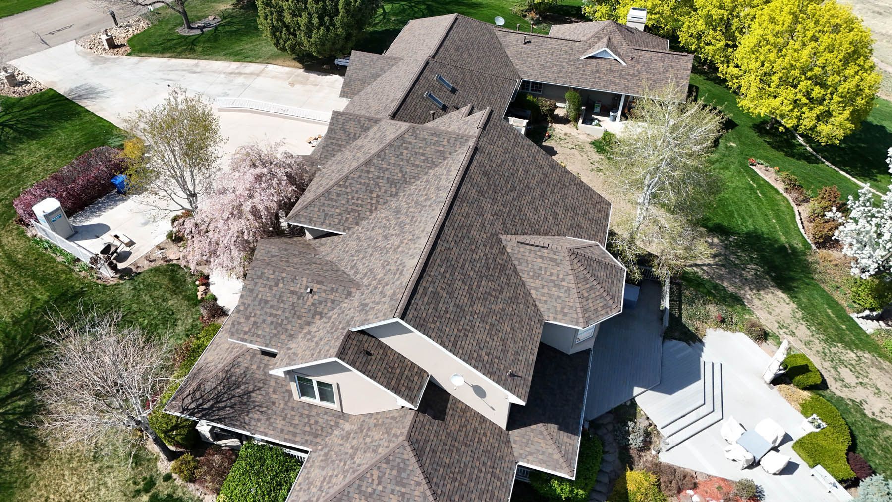 Aerial view of a large brown-roofed house with a light-colored exterior and surrounding green lawn.