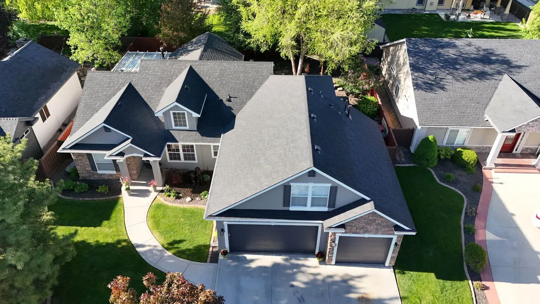 Aerial view of a gray house with a dark roof and two-car garage, surrounded by green grass and trees.