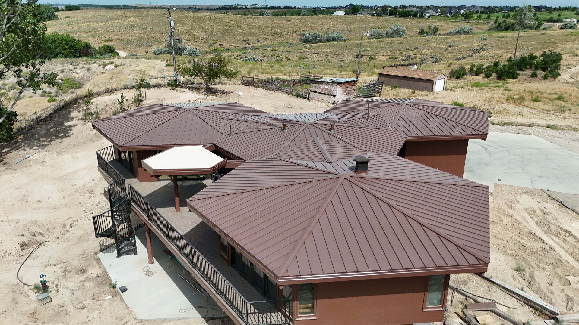 Aerial view of a brown-roofed house with a patio umbrella in a dry, open landscape