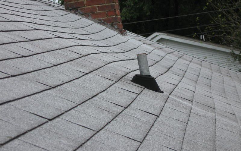 Rooftop with gray shingles and a small vent pipe near a brick chimney