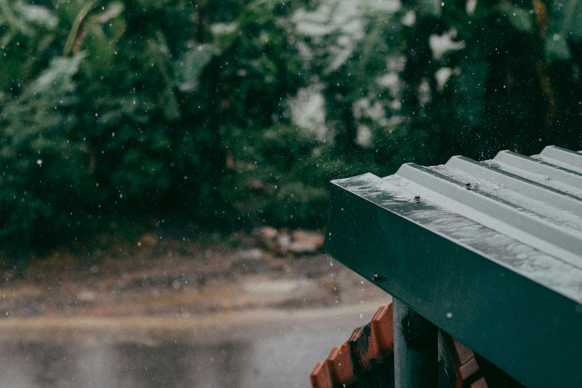 Rain falling on a green-roofed structure with blurred trees in the background