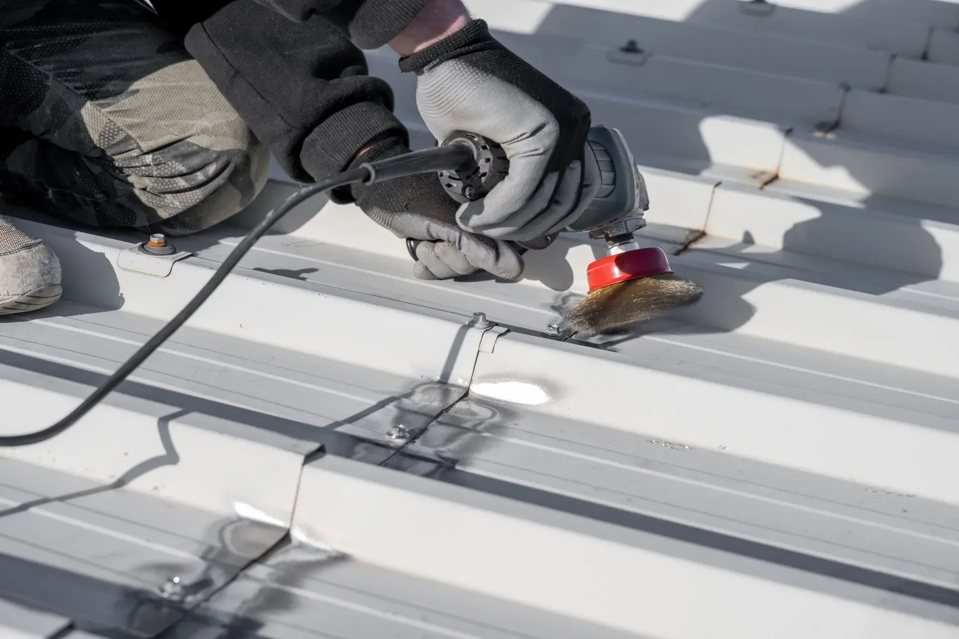 Worker using a power tool on a white metal roof panel during installation