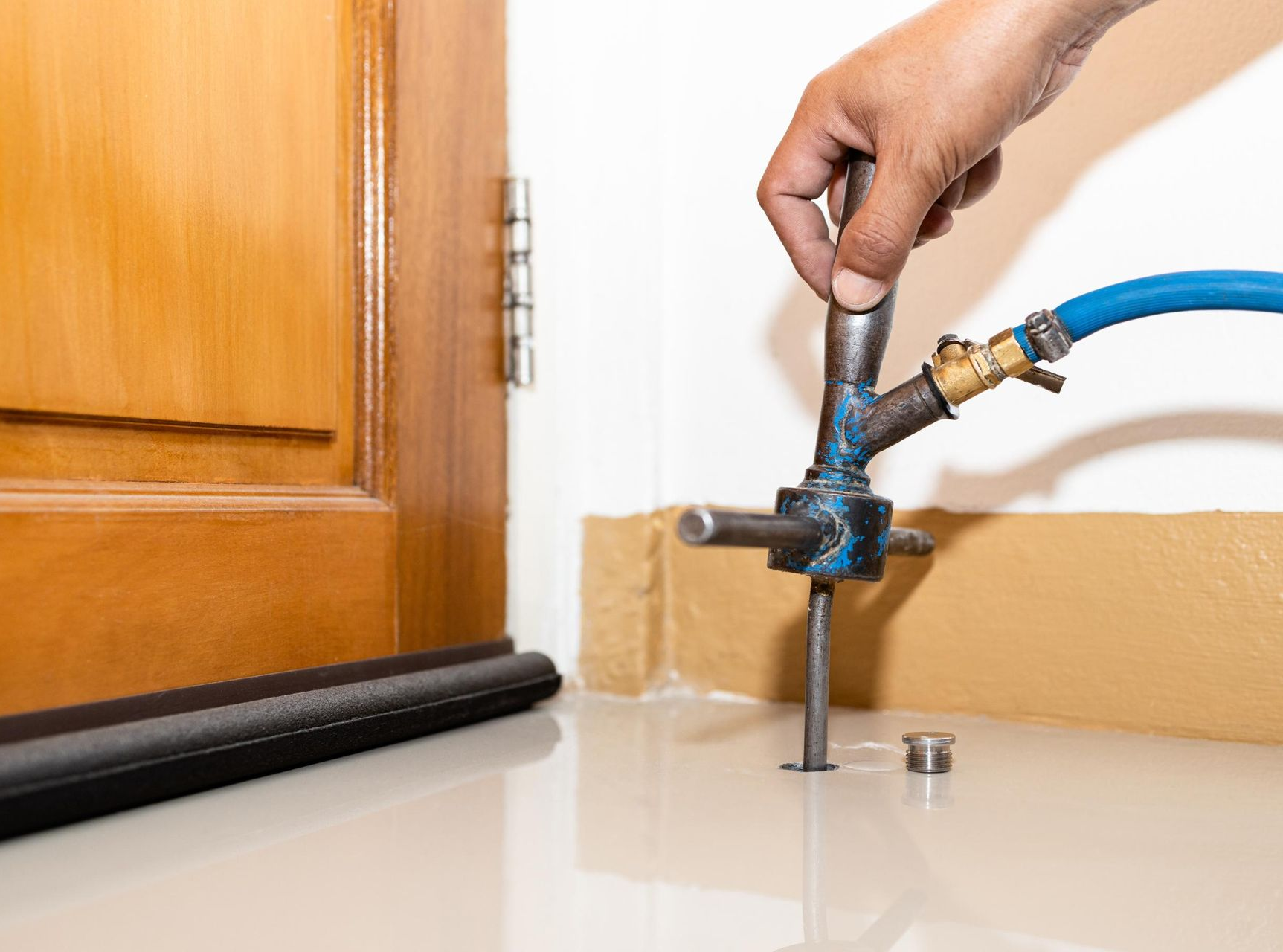 A person uses a specialized nozzle tool to inject pest control chemicals into a hole drilled in a tile floor near a door.