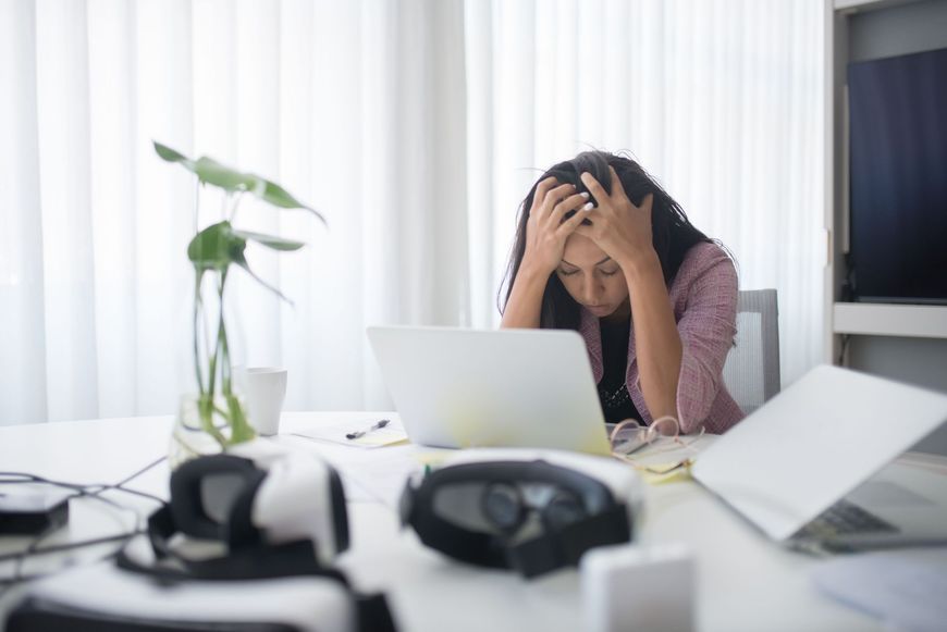 Stressed person at a desk with a laptop, head in hands, in a bright office