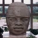 A statue of a man 's head is sitting on a table in front of a window.