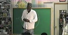 A man is standing in front of a green chalkboard in a room.