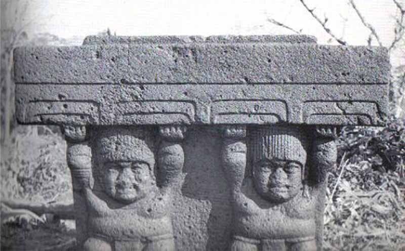 A black and white photo of two statues holding a large stone block.