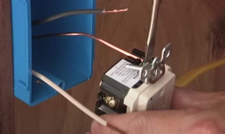 A person is fixing a light switch with a screwdriver.