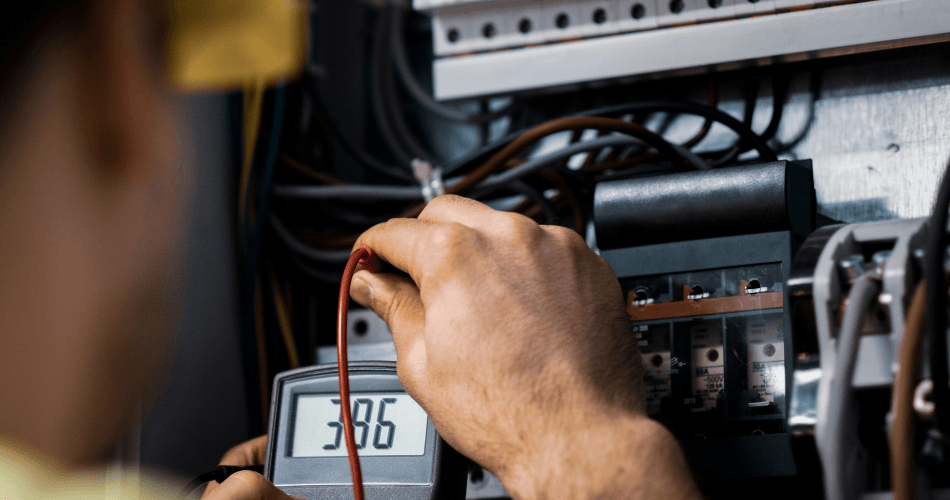 A man is using a digital multimeter to test an electrical box.