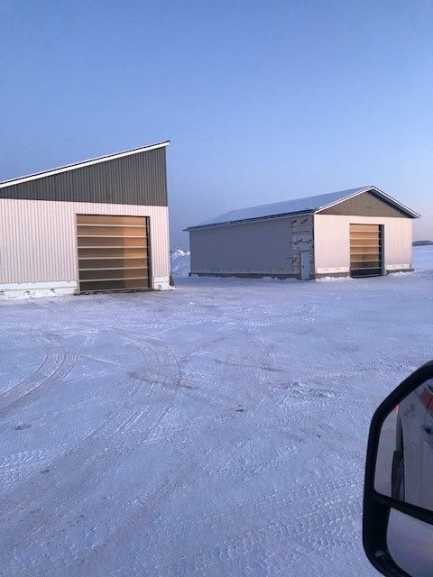 Deux bâtiments de stockage en métal gris se dressent sur un champ enneigé sous un ciel bleu azur.