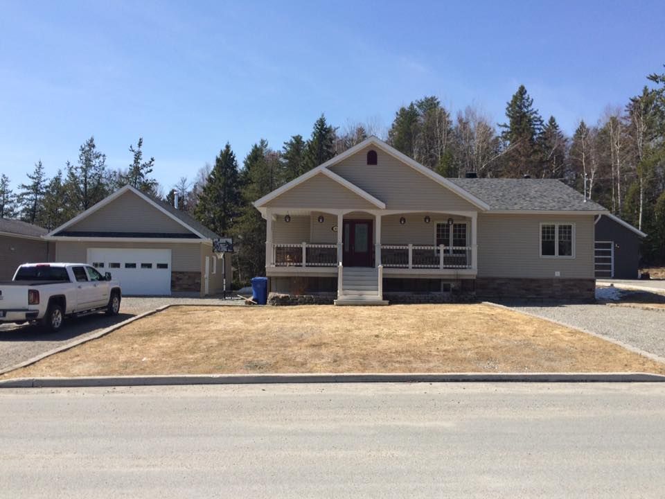 Une maison de plain-pied beige avec un porche, un garage attenant sur la gauche et une camionnette blanche garée dans l'allée.