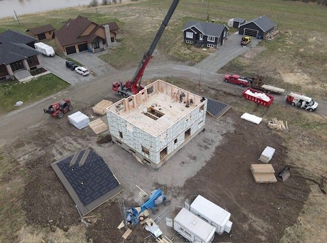 Vue aérienne d'un chantier de construction avec une grue rouge et des maisons environnantes.