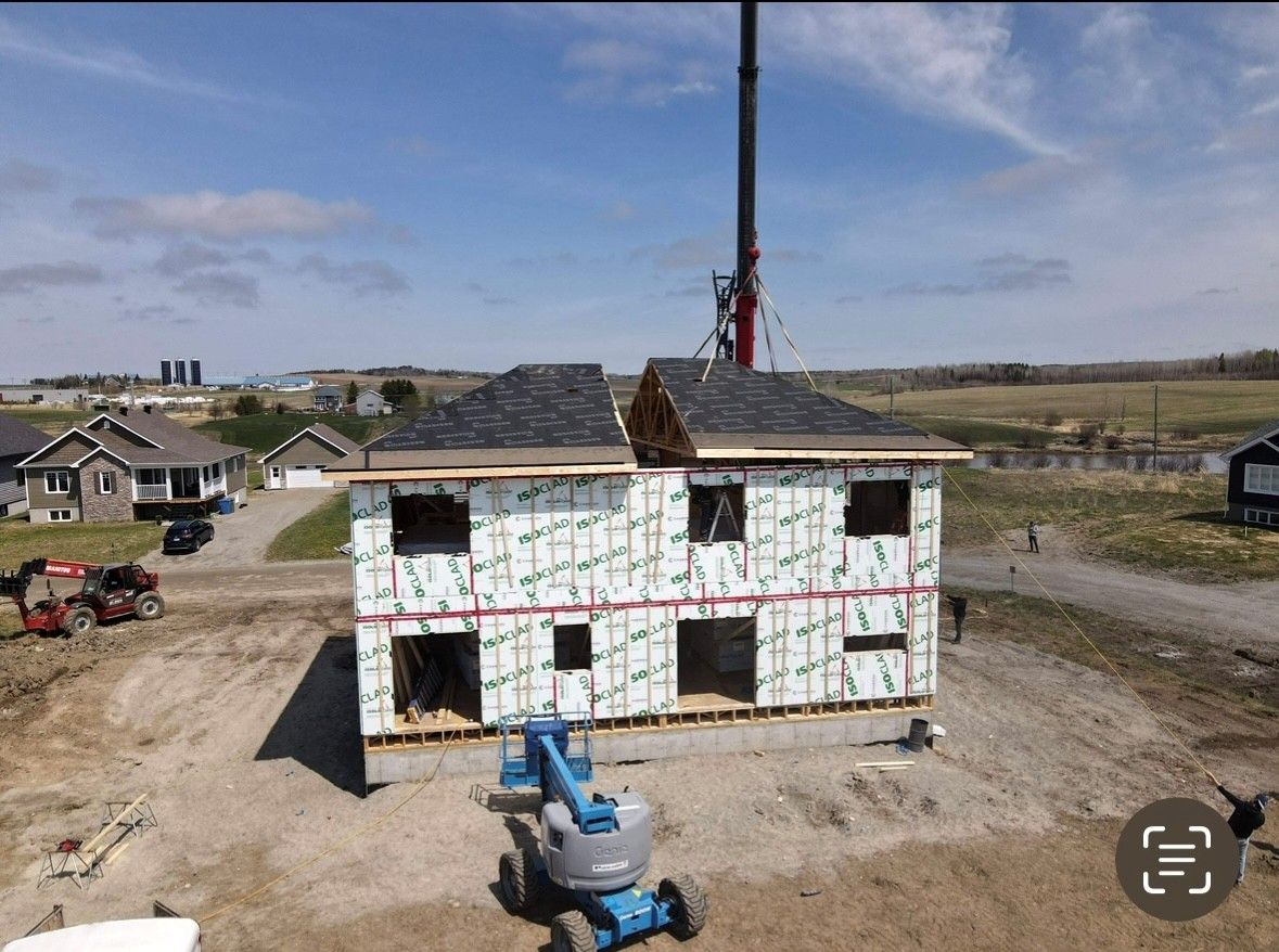 Une grue dépose un module de maison sur une structure à deux étages en construction dans un champ.