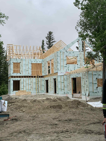 Une maison à ossature bois de deux étages en construction, recouverte de panneaux d'isolation extérieure bleu clair.