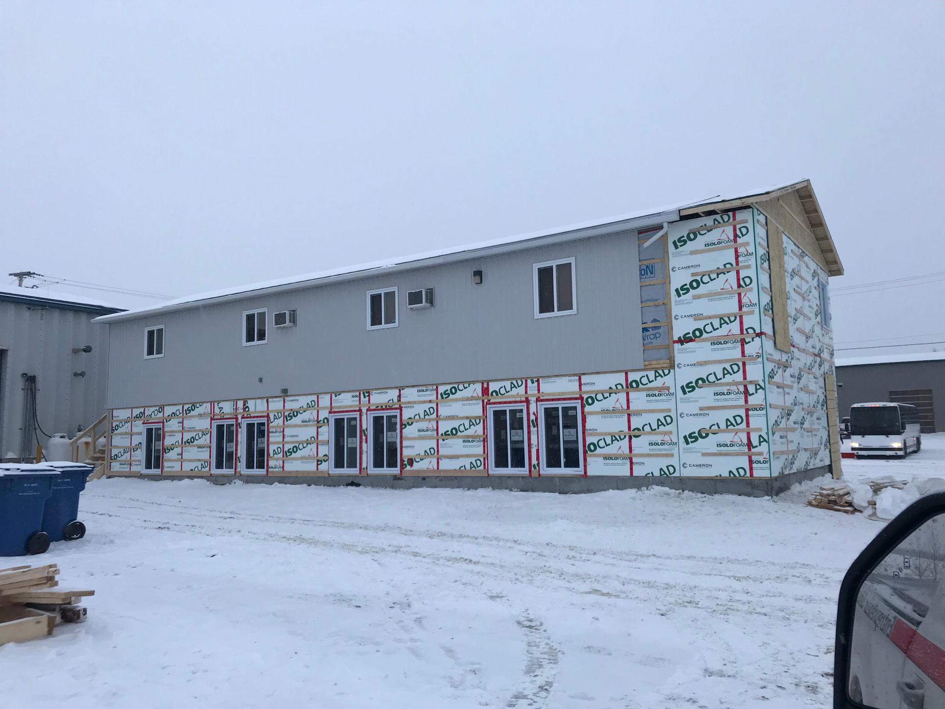 Un bâtiment de deux étages en construction, avec un bardage gris à l'étage supérieur et une isolation apparente à l'étage inférieur.