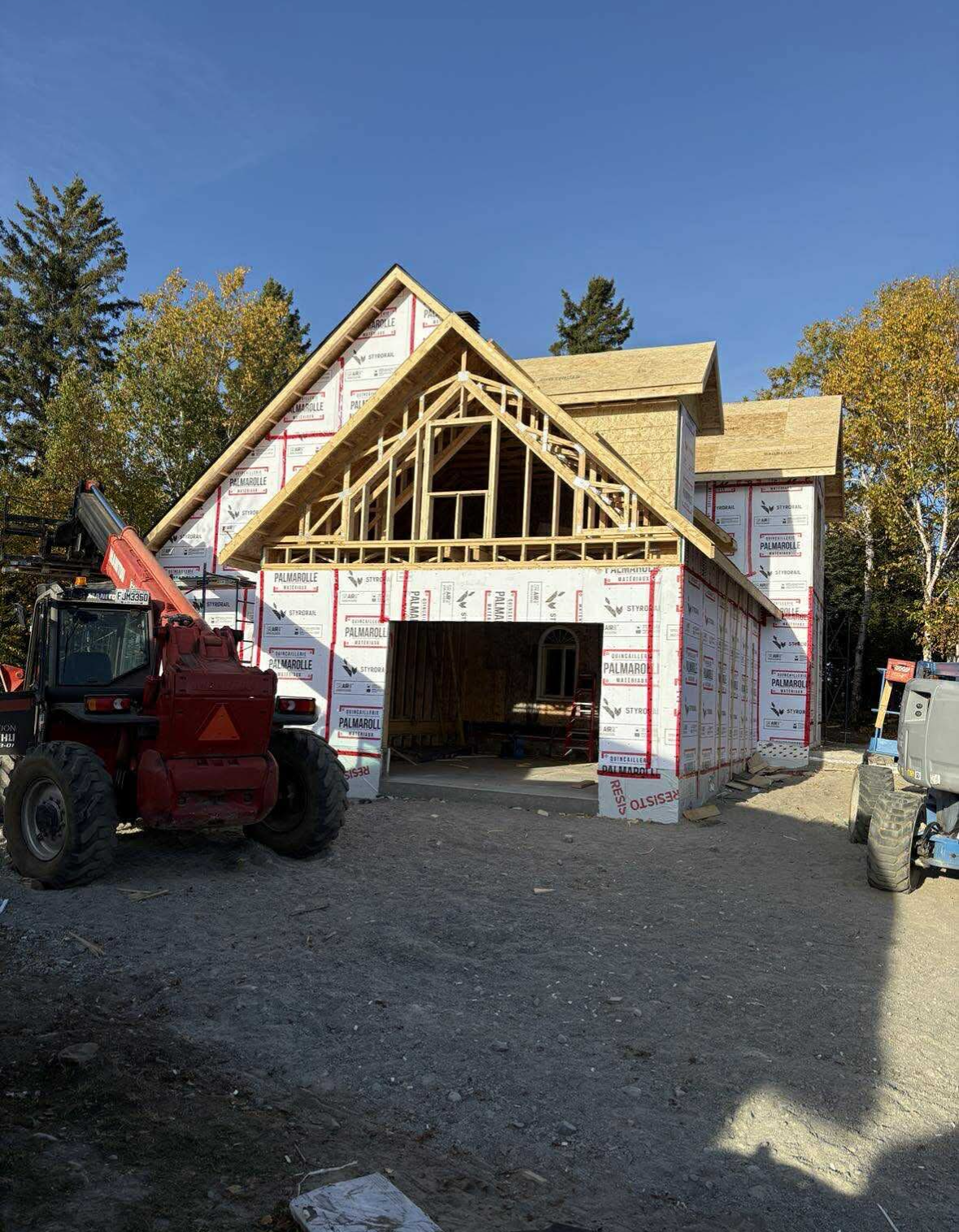 Construction d'un bâtiment à ossature bois de deux étages avec un revêtement extérieur blanc et un chariot télescopique rouge garé devant.