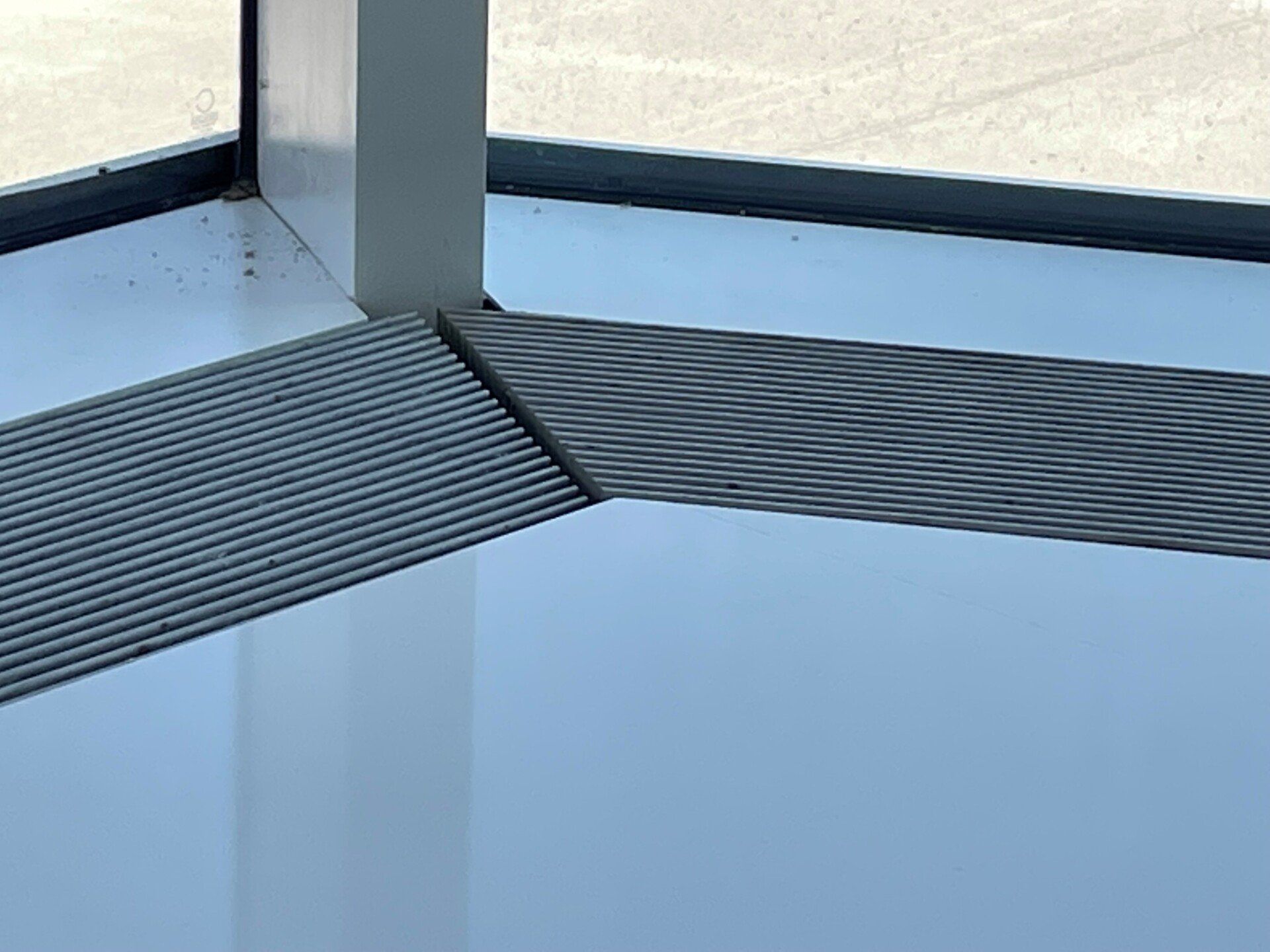 A corner of a room with a window and a mat on the floor.