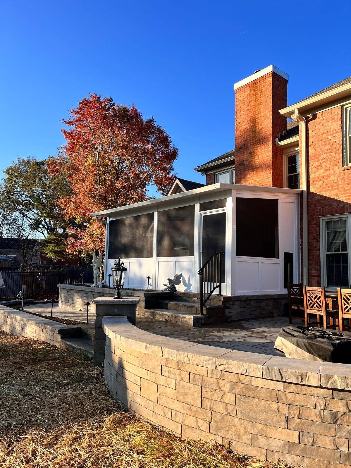 A brick house with a screened in porch and a stone wall in front of it.