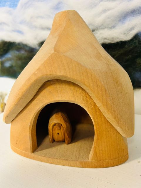 Small wooden birdhouse with a tiny bird inside, on a white surface outdoors.