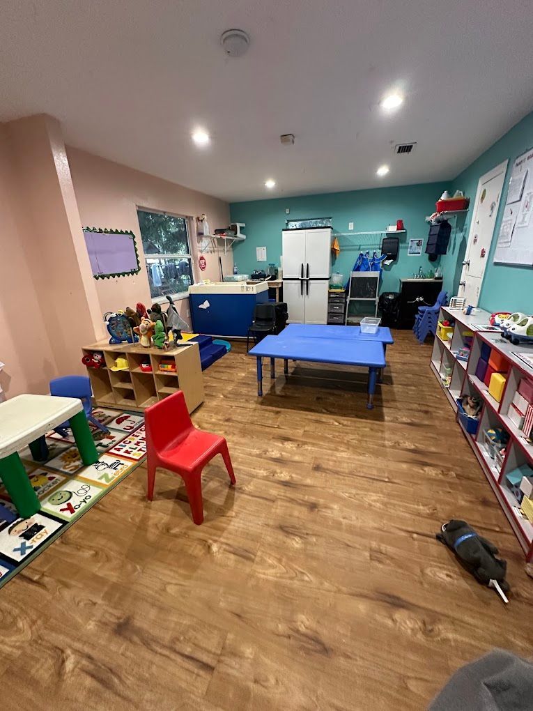 A classroom with tables , chairs , shelves and a vacuum cleaner.