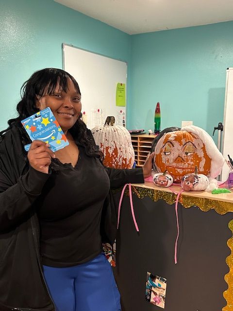 A woman is holding a card in front of a pumpkin.