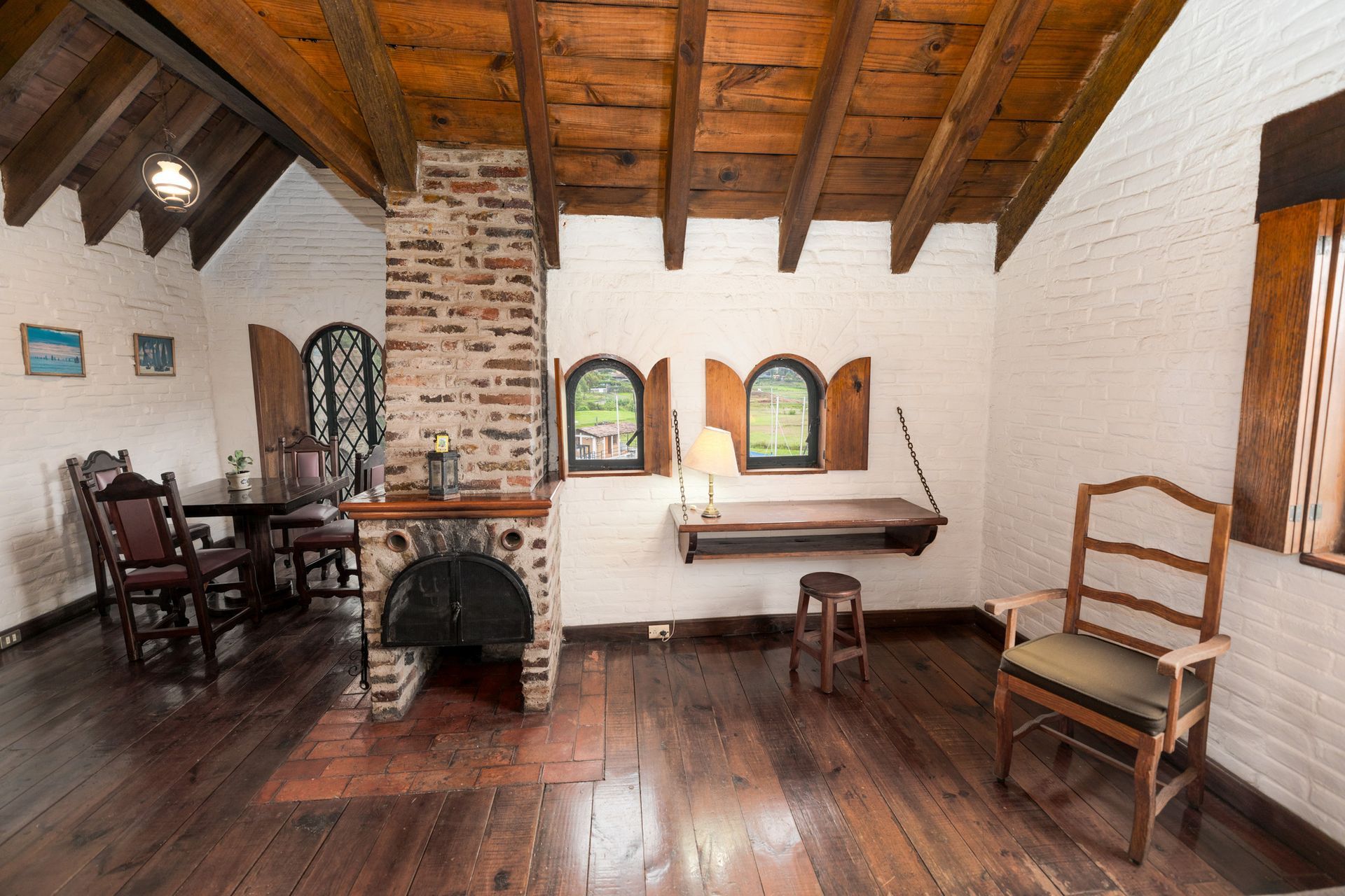 Habitación rústica con vigas de madera, chimenea de ladrillo, muebles antiguos y suelo de madera oscura.