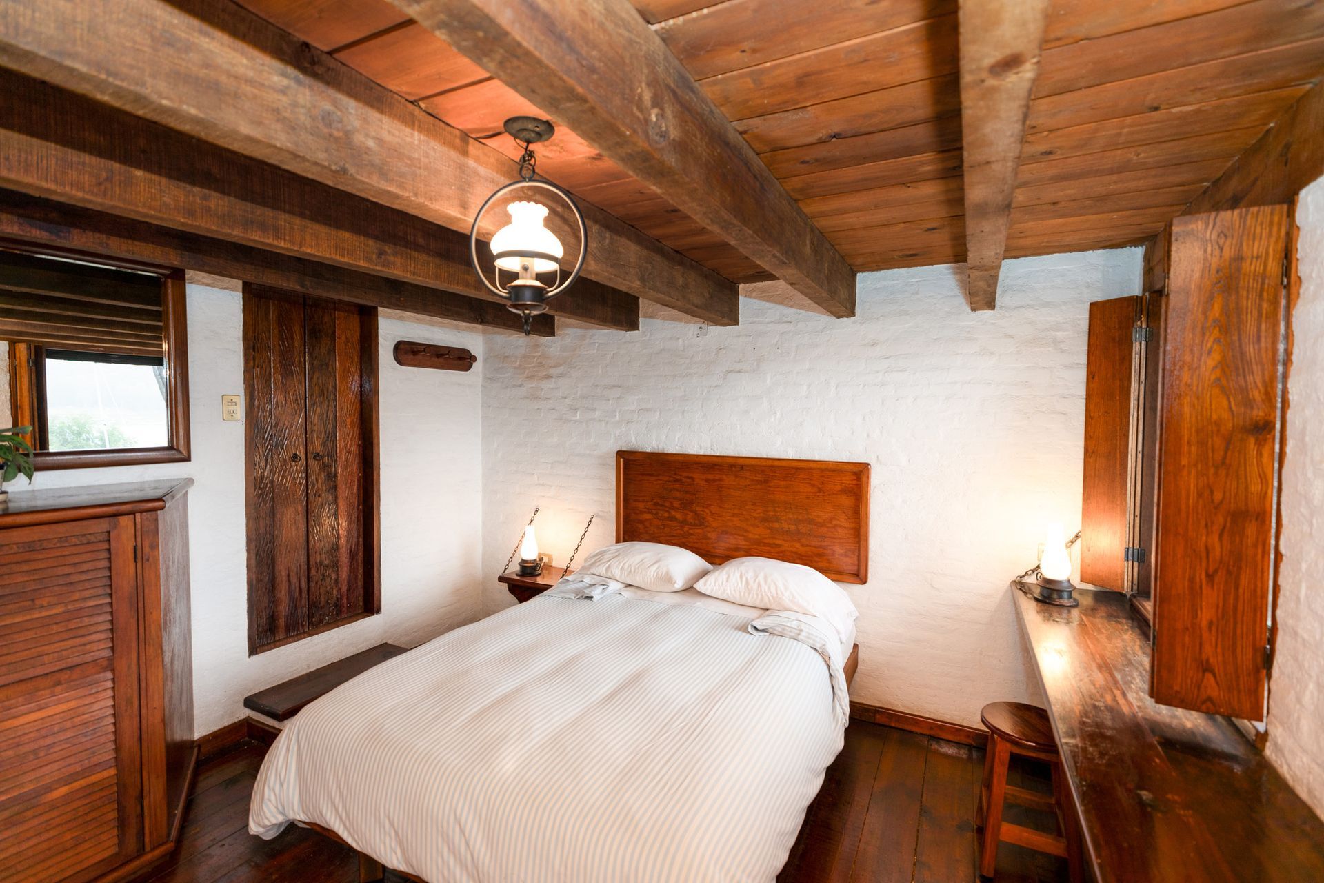 Acogedor dormitorio rústico con vigas de madera, cama blanca y paredes revestidas de cálidos paneles de madera.