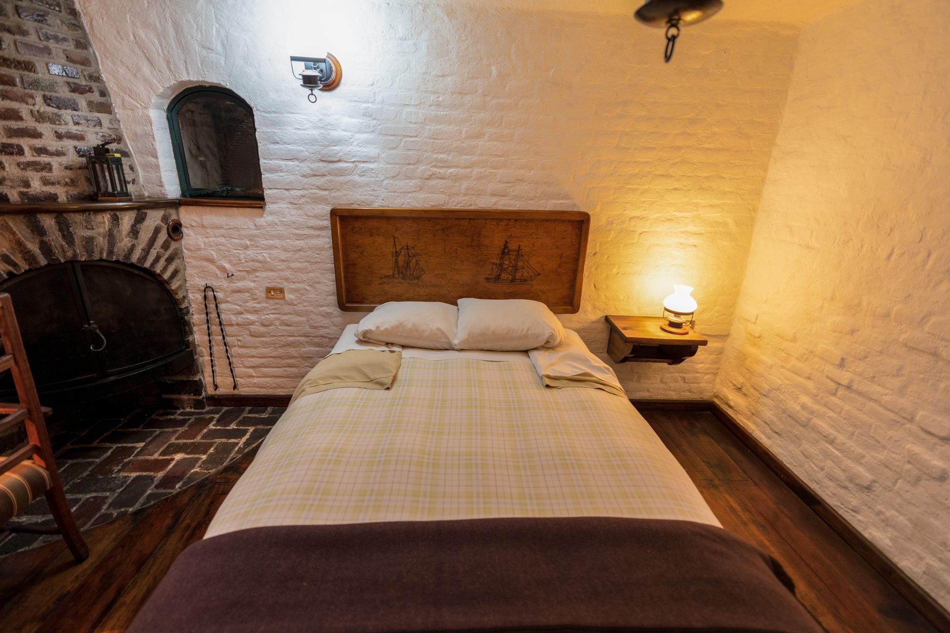 Acogedora habitación con cama, chimenea de ladrillo y cálida iluminación de lámparas sobre paredes blancas.