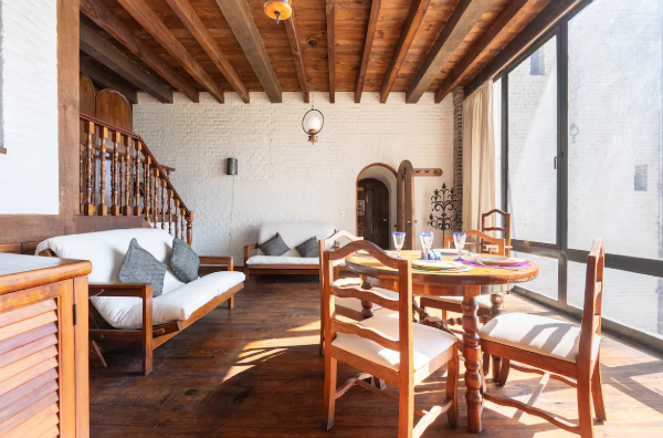 Acogedora sala de estar rústica con sofás blancos, vigas de madera y una mesa de comedor junto a una puerta arqueada.